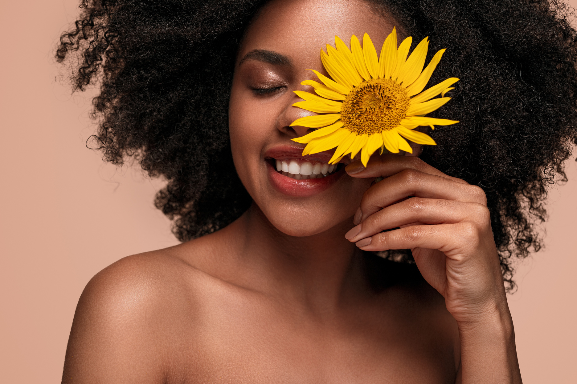 Happy African American woman touching face with flower